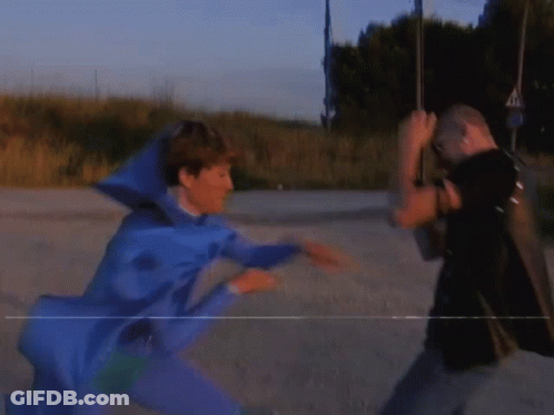 A Man In A Blue Costume Is Fighting Another Man In A Black Shirt GIF