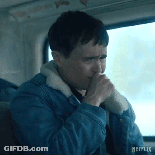 A Man In A Blue Denim Jacket Is Coughing While Sitting In Front Of A Window . GIF