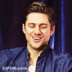 A Man In A Blue Denim Jacket Is Smiling With His Eyes Closed . GIF