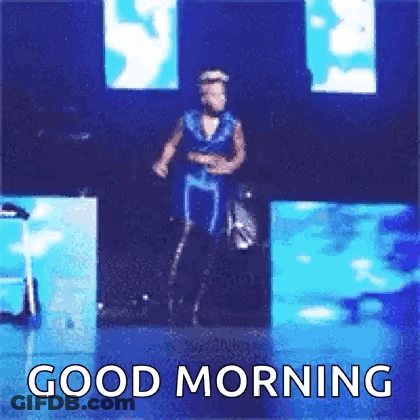 A Man In A Blue Dress Is Dancing On A Stage With The Words `` Good Morning '' Below Him . GIF
