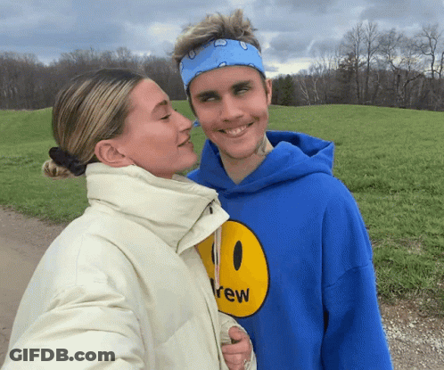A Man In A Blue Drew Hoodie Kisses A Woman GIF