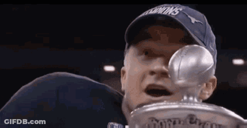 A Man In A Blue Hat Is Holding A Trophy In His Hand . GIF