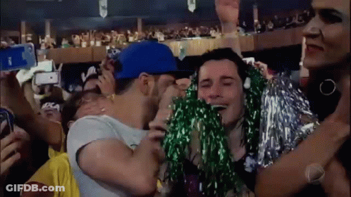 A Man In A Blue Hat Is Kissing A Woman In A Crowd . GIF
