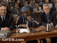 A Man In A Blue Hat Is Sitting At A Table With Other Men GIF