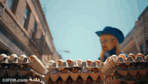 A Man In A Blue Hat Is Standing Behind A Stack Of Eggs GIF