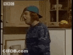 A Man In A Blue Hat Is Standing In A Kitchen . GIF