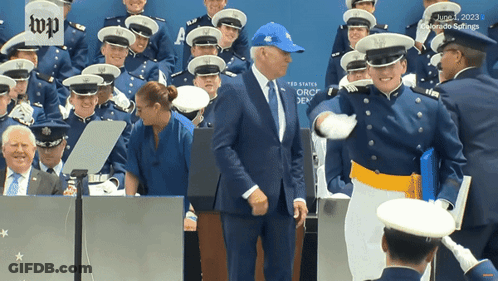 A Man In A Blue Hat Is Standing In Front Of A Group Of Military Men GIF