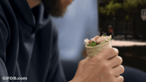 A Man In A Blue Hoodie Is Holding A Wrap In His Hands GIF