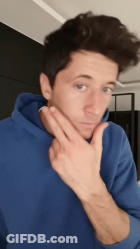 A Man In A Blue Hoodie Is Making A Funny Face While Holding His Hand To His Chin . GIF