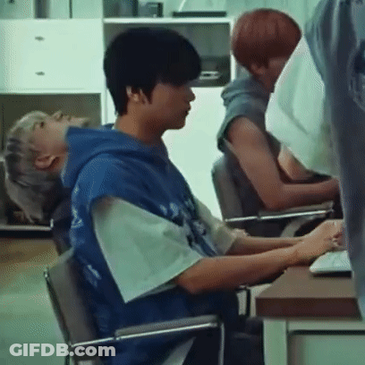 A Man In A Blue Hoodie Is Sitting In A Chair In Front Of A Computer . GIF