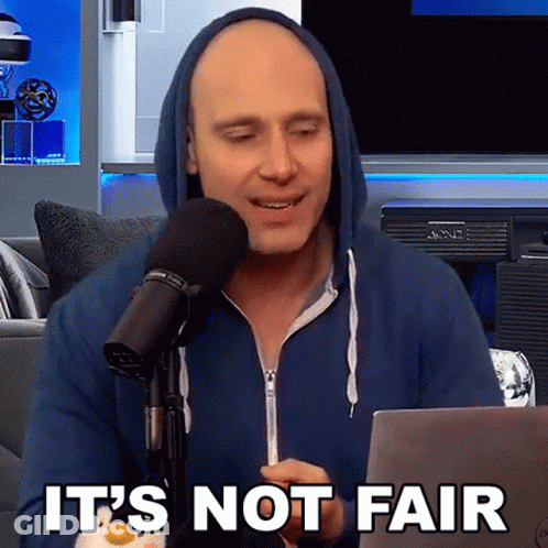 A Man In A Blue Hoodie Is Sitting In Front Of A Microphone With The Words " It 'S Not Fair " On The Bottom GIF