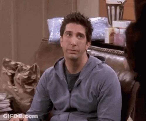 A Man In A Blue Hoodie Is Sitting On A Couch And Looking At The Camera . GIF
