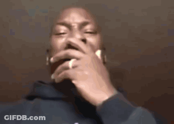 A Man In A Blue Hoodie Is Smoking A Cigarette With His Hand On His Mouth . GIF