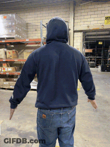 A Man In A Blue Hoodie Is Standing In A Warehouse With His Arms Outstretched In Front Of A Sign That Says Exit GIF