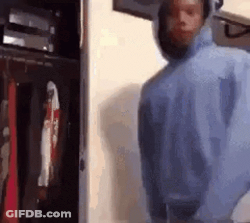 A Man In A Blue Hoodie Is Standing In Front Of A Closet With Clothes Hanging On It . GIF