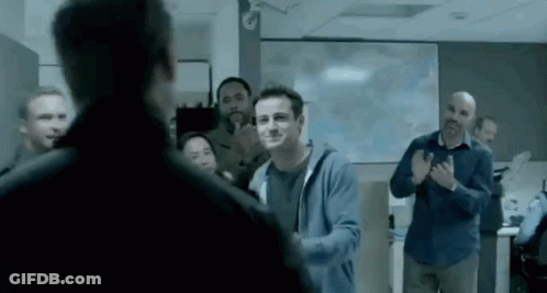 A Man In A Blue Hoodie Is Standing In Front Of A Group Of People Applauding . GIF