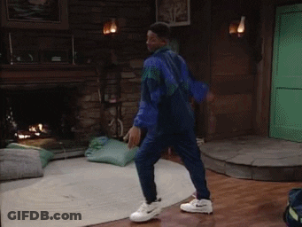 A Man In A Blue Jacket And White Nike Shoes Is Dancing In A Living Room GIF