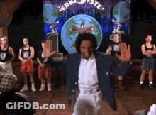 A Man In A Blue Jacket And White Pants Is Dancing On A Stage In Front Of A Crowd . GIF