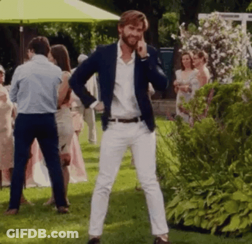 A Man In A Blue Jacket And White Pants Is Standing In A Grassy Field Talking On A Cell Phone . GIF