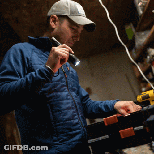 A Man In A Blue Jacket Holds A Flashlight In His Hand GIF
