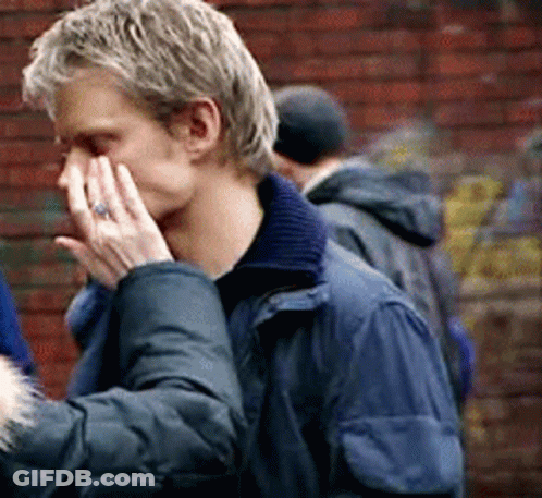 A Man In A Blue Jacket Is Covering His Face With His Hands GIF