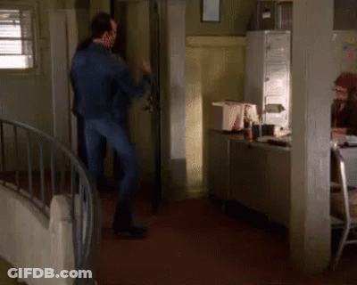 A Man In A Blue Jacket Is Dancing In A Room With A Spiral Staircase GIF