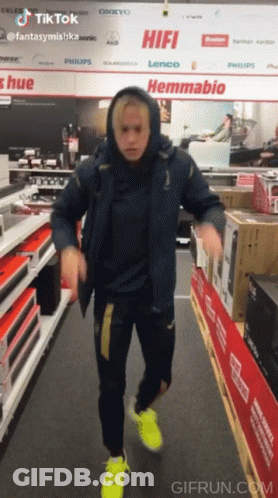 A Man In A Blue Jacket Is Dancing In A Store With A Sign That Says Hifi GIF