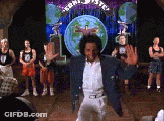 A Man In A Blue Jacket Is Dancing In Front Of A Sign That Says ' Jerk ' GIF