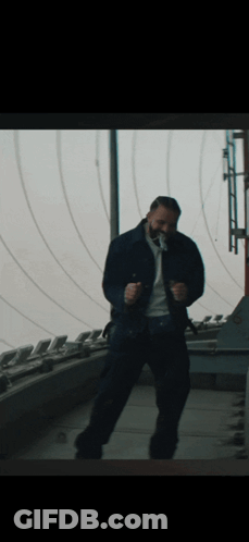 A Man In A Blue Jacket Is Dancing In Front Of A Window GIF