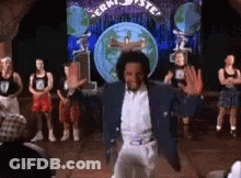 A Man In A Blue Jacket Is Dancing On A Stage In Front Of A Crowd Of People . GIF