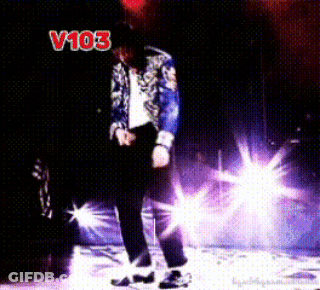 A Man In A Blue Jacket Is Dancing On A Stage In Front Of A Sign That Says " V103 " GIF
