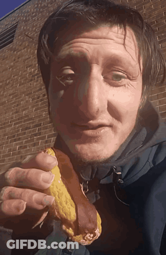 A Man In A Blue Jacket Is Eating A Sandwich GIF