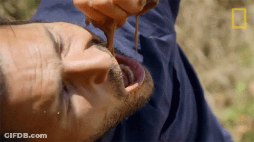 A Man In A Blue Jacket Is Eating Something With A National Geographic Logo In The Corner GIF