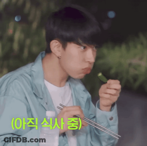 A Man In A Blue Jacket Is Eating Something With Chopsticks And A Bottle Of Water GIF