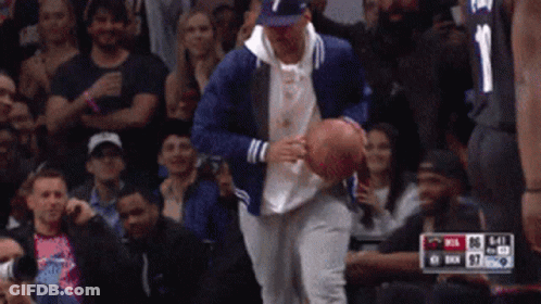 A Man In A Blue Jacket Is Holding A Basketball In Front Of A Crowd Of People GIF