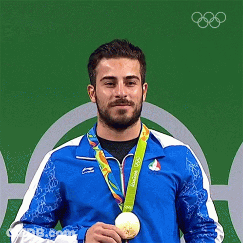 A Man In A Blue Jacket Is Holding A Gold Medal From The Olympics GIF