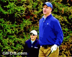 A Man In A Blue Jacket Is Holding A Golf Club While Another Man Watches GIF