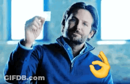 A Man In A Blue Jacket Is Holding A Piece Of Paper In His Hand And Making An Ok Sign . GIF