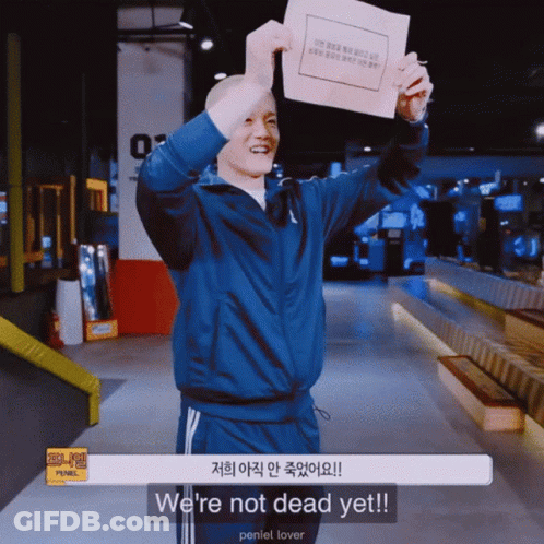 A Man In A Blue Jacket Is Holding Up A Piece Of Paper That Says We 'Re Not Dead Yet GIF