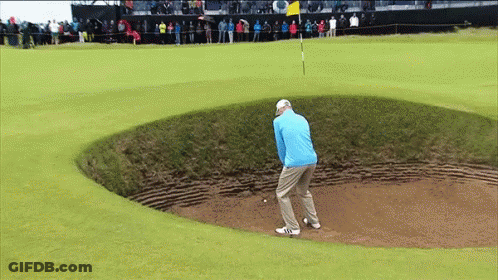A Man In A Blue Jacket Is Playing Golf In A Bunker GIF