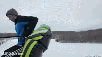 A Man In A Blue Jacket Is Pulling Another Man On A Sled GIF