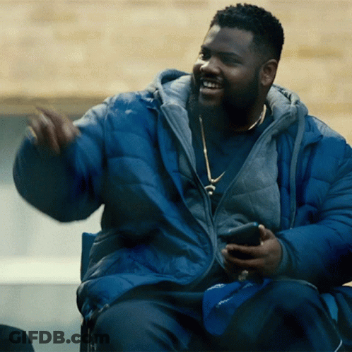 A Man In A Blue Jacket Is Sitting In A Chair Holding A Cell Phone GIF