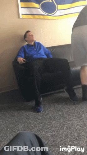 A Man In A Blue Jacket Is Sitting On A Black Couch In Front Of A Banner That Says Tm GIF