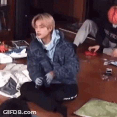 A Man In A Blue Jacket Is Sitting On The Floor In A Living Room With Other People . GIF