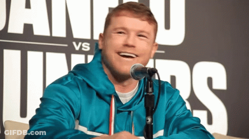 A Man In A Blue Jacket Is Smiling In Front Of A Microphone In Front Of A Sign That Says Vs GIF