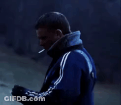 A Man In A Blue Jacket Is Smoking A Cigarette While Standing In The Dark . GIF