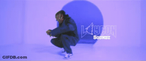 A Man In A Blue Jacket Is Squatting Down In Front Of A Purple Background That Says K19con GIF