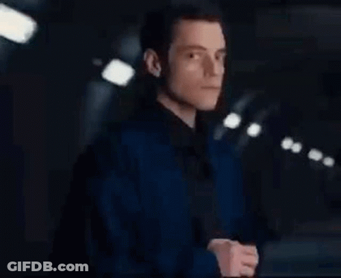 A Man In A Blue Jacket Is Standing In A Dark Room . GIF