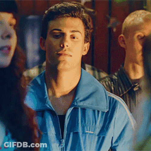 A Man In A Blue Jacket Is Standing In Front Of A Crowd Of People . GIF