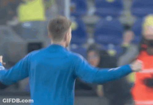 A Man In A Blue Jacket Is Standing In Front Of A Crowd With His Fist In The Air GIF